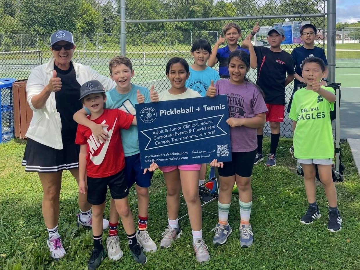 Junior campers holding a Universal Rackets sign with their coach